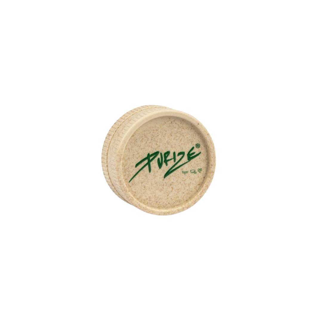 PURIZE® Hemp Grinder 55mm, valmistettu tummanvihreästä hamppukomposiitista, asetettuna luonnonmukaiseen ympäristöön.