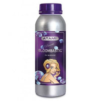 Atami Bloombastic 100ml -ravinnepullo vihreiden, kukkivien kasvien edessä, kuvastaen tuotteen tehoa ja satoa.