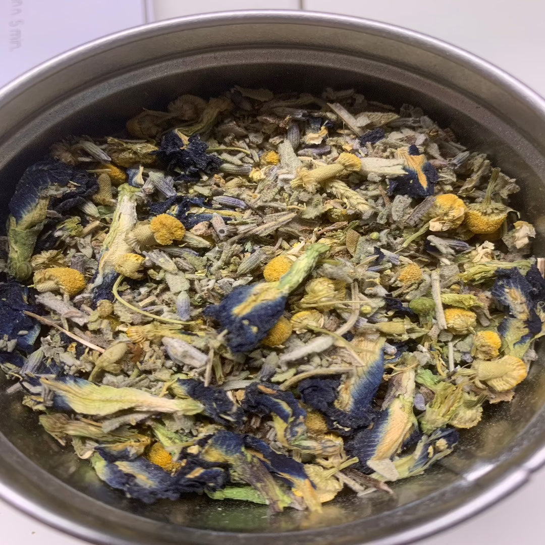 Kuva Yrttisessio Nukkumatin Sininen 8g -yrttisekoituspussista tai purkista, jossa näkyy hienojakoisia sinertäviä yrttejä ja makuuhuoneen rentouttava tunnelma taustalla.