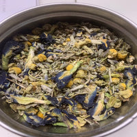 Kuva Yrttisessio Nukkumatin Sininen 8g -yrttisekoituspussista tai purkista, jossa näkyy hienojakoisia sinertäviä yrttejä ja makuuhuoneen rentouttava tunnelma taustalla.