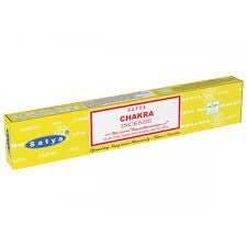 Kuva Satya Chakra suitsuketikuista savuamassa tummalla taustalla, taustalla heikosti näkyvissä chakrasymboleja edustava grafiikka