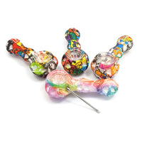 Värikäs monivärinen silikonipiippu, jossa integroitu dabber-työkalu ja diskreetti säilytyslokero pohjassa. Näkyvillä vesisiirtokuviointi.