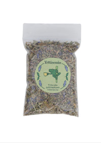 Yrttisessio 8g Vihreän Pyhimyksen Vierailu -yrttisekoituspussi, jossa näkyy kuivattuja mintunlehtiä ja damianaa. Pussi on valko-vihreä ja aseteltu luonnonläheiselle puupinnalle.